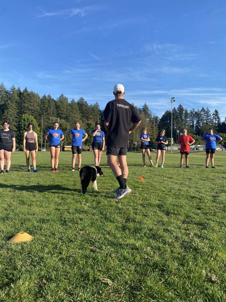 A coach talking to a line of junior players at training on the Juan de Fuca field
