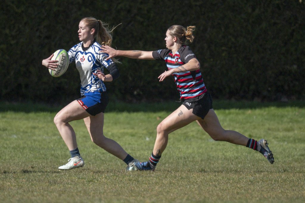 A Westshore Valkyrie at full stride with the ball, a Castaway Wanderers defender reaching for her, February 2026.