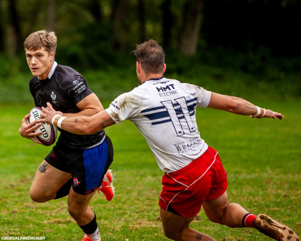 A Westshore player in the black away jersey fending a Ravens defender, ball under his arm, fall 2025.